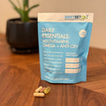 A weekly pouch labeled 'Daily Essentials: Multivitamins Omega + Anti-Oxy' from ShiftSetGo, containing packets of supplements, displayed on a wooden surface with a plant in the background.